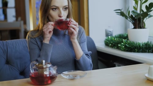 Beautiful Woman Dreaming, Smiling with Cup of Tea at Window in Cafe