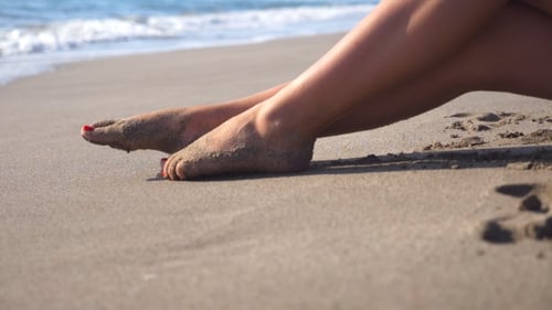 Beautiful Female Legs Lying on Sand and Relaxing Near Sea Shore. Young Woman Sitting on the Coast