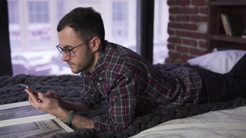 Man Relaxing on Bed Using Smartphone Indoors