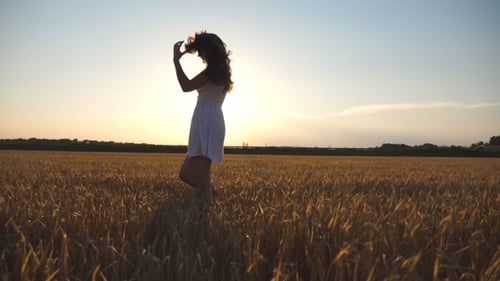 Beautiful Girl is Walking along Wheat Field
