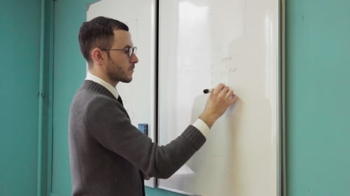 Young Adult Teacher Writes Formulas on Whiteboard
