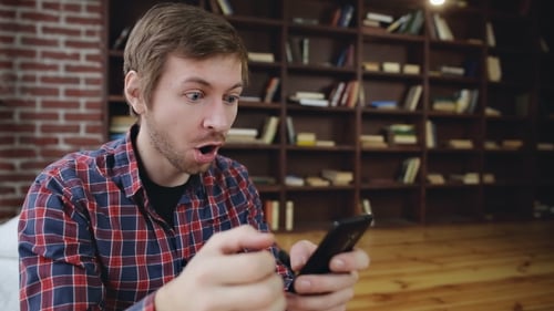 Excited Young Man Cheering While Looking at Phone