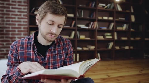 Man Reading Book in Front of Bookshelf