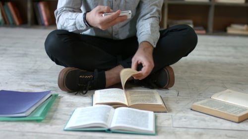Student with Phone Making Cheat Sheet in Library