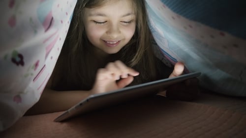 Petite fille utilise une tablette numérique sous couverture, la nuit