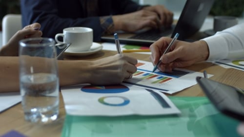 Hands Writing on Various Financial Charts on Table