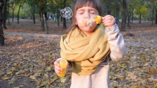 Little Girl Blowing Bubbles in a Fall Park
