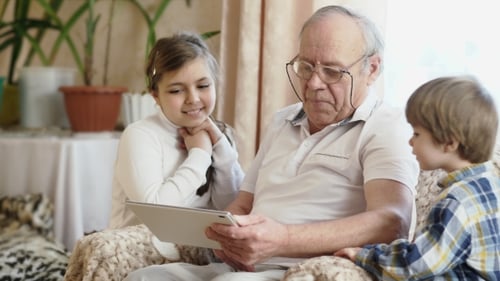 Senior Man Using Tablet with Children Indoors