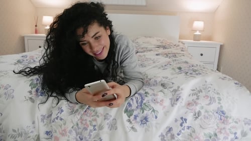Woman Lies on Bed Looking at Phone