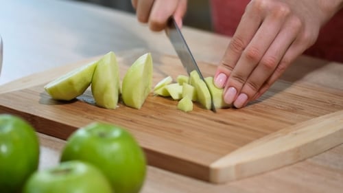 Frau mit Messer schneidet Apfel auf Schneidebrett