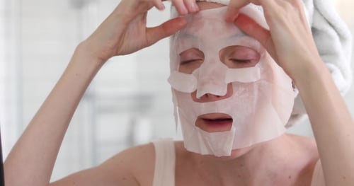 Woman Applying Mask on Her Face Looking in Mirror