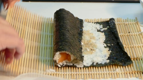 Person Making a Sushi Roll with Bamboo Mat
