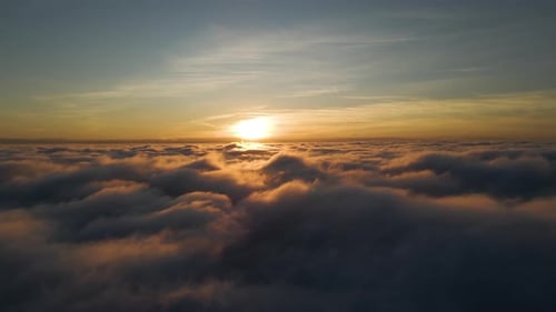 Aerial view of bright yellow sunset over white dense clouds with blue sky overhead.