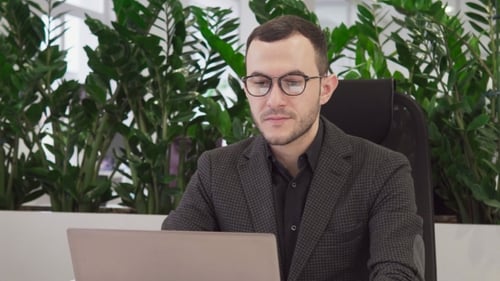 Young Business Man with Glasses Looks at the Laptop Screen