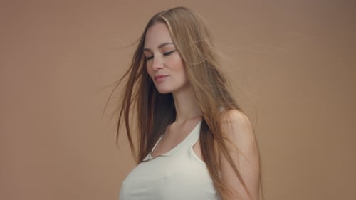 Beauty Woman Model in Studio on Beige Background with Wind in Hair Bllowing It