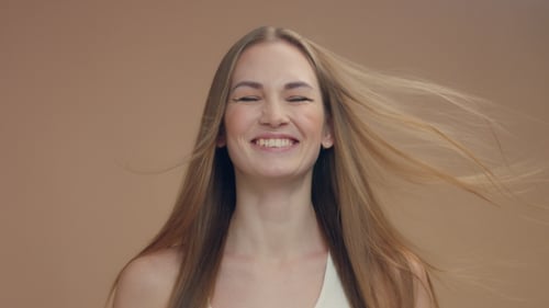 Beauty Woman Model in Studio on Beige Background with Wind in Hair Bllowing It