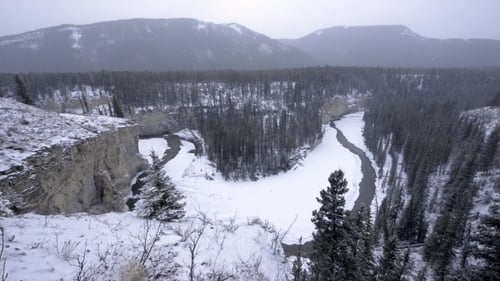 Icy Winter River Winds Through Canyon Valley in Snowstorm