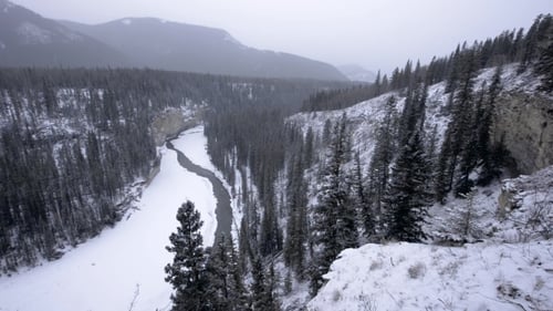 Icy Winter River Winds Through Canyon Valley in Snowstorm