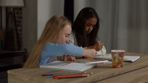 Two Girls Painting Together at Table Indoors