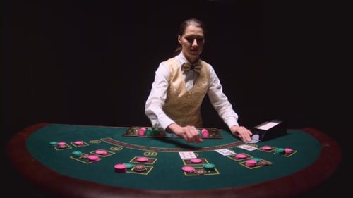 Casino Dealer Pulls Cards From Card Holder, Lays Chips at a Poker Table. Black Background.