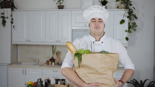 Smiling Chef Holding Groceries in Bright Kitchen
