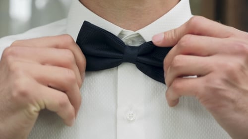 Man adjusts black bow tie on white shirt
