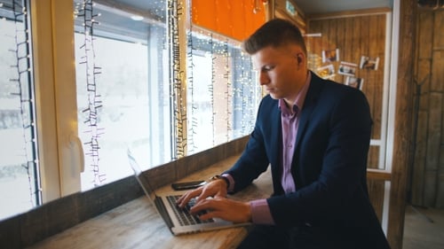 Working From Cafe. Cheerful Young Man in Smart Casual Wear Looking at Laptop and Sitting Near Window