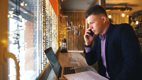 a Young Businessman Talking on the Phone and Working at a Laptop in a Cafe
