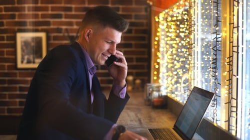 a Young Businessman Talking on the Phone and Working at a Laptop in a Cafe