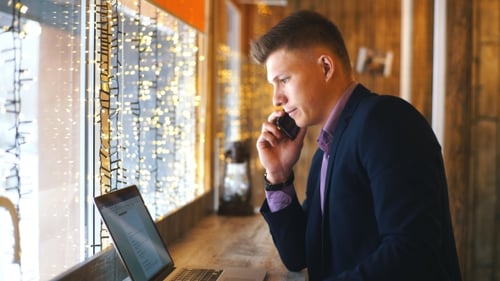 a Young Businessman Talking on the Phone and Working at a Laptop in a Cafe
