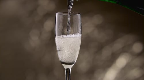 Half Empty Glass Is Filled with Champagne Green Bottle. Bokeh Background