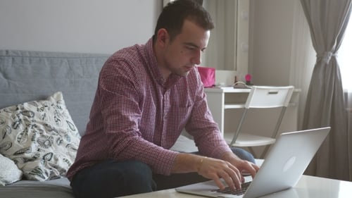 Eine Person arbeitet von zu Hause aus mit der Oberseite und dem Trackpad. Junger Geschäftsmann sitzt am Tisch und trinkt