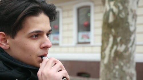 Un jeune homme se tient dehors et fume une cigarette électronique en hiver