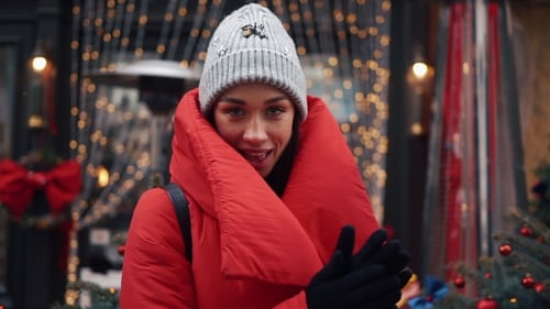 Smiling Woman Dances Before a Door with Christmas Decor on the Street of an Old City