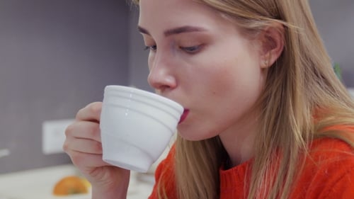 Portrait of Beautiful Caucasian Girl in Red Sweater Drinks Coffee