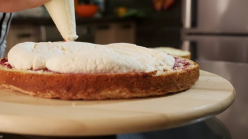 of Putting Cream on a Sponge Cake. Cake on a Rotating Stand.