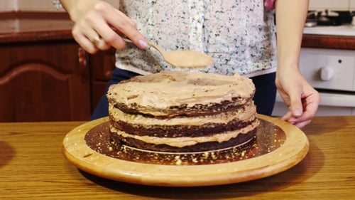 Woman Frosting Chocolate Cake in a Kitchen