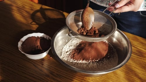Woman Sieves Cocoa Powder into Bowl for Baking
