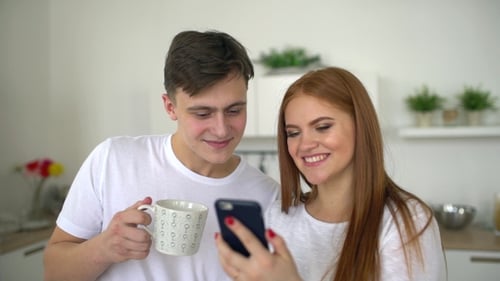 Smiling Couple Looking at Phone in Kitchen Together
