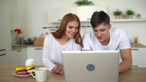 Smiling Couple Watching Laptop Screen in Modern Kitchen