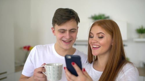Young Couple Looking at Phone Together in Bright Kitchen