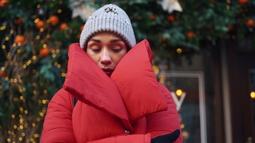 Girl in Red Jacket Tries To Warm Herself Standing on the Street with Christmas Decor