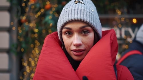 Girl in Red Jacket Tries To Warm Herself Standing on the Street with Christmas Decor