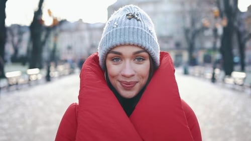 Portrait of a Stunning Girl in Grey Hat and Red Coat Smiling While She Stands on the Street Before