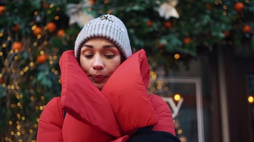 Girl in Red Jacket Tries To Warm Herself Standing on the Street with Christmas Decor