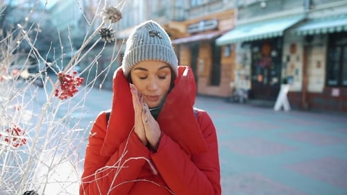 Girl in Red Winter Jacket Tries To Warm Herself Standing on the Street Covered with Snow