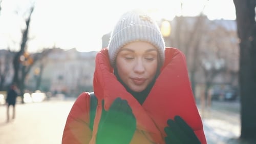Beautiful Woman in a Red Jacket Stands on the Street Covered with Snow in a Sunny Winter Day