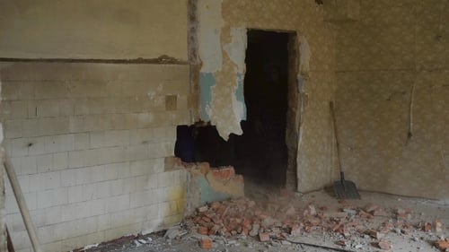 El constructor está rompiendo una pared en un viejo piso, golpeando con un mazo en un sitio de construcción, ladrillos