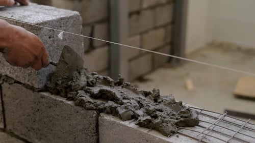 Arbeiter trägt Zementmörtel auf eine Wand auf, um Bausteine zu verlegen, gleichmäßig zu verteilen