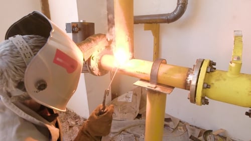 Worker Welding Yellow Pipes Together